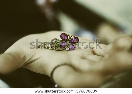 Right hand with ring holding a golden hair clip shaped like a pink butterfly with three shiny. Royalty-Free Stock Photo #576890809