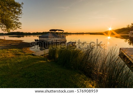 View of lake sunrise showing docked pontoon boat Royalty-Free Stock Photo #576908959