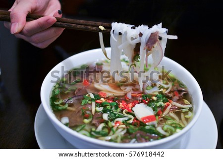 Girl eating traditional Vietnamese beef soup Pho Bo with chopsticks Royalty-Free Stock Photo #576918442