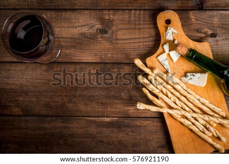 Red wine and snacks for it: Italian grissini bread sticks and blue cheese on a cutting wooden board on a wooden table, top view, copy space 