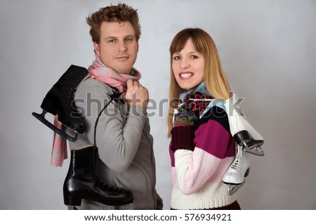 Young woman and man holding ice skates for winter sport in front of grey background 