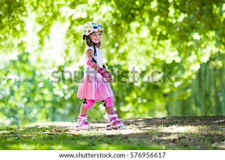 Little girl learning to roller skate in sunny summer park. Child wearing protection elbow and knee pads, wrist guards and safety helmet for safe roller skating ride. Active outdoor sport for kids