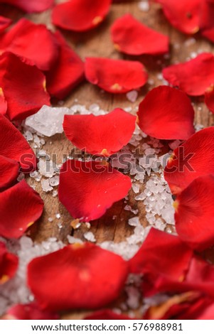 Red roses petals with pile of salt on old wooden board