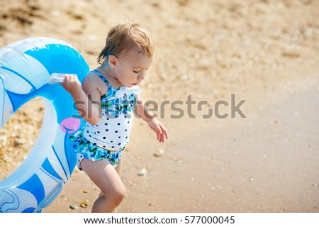 Little girl in swim suit with swimming circle ready to go into the sea at early sunset. Summer fun.