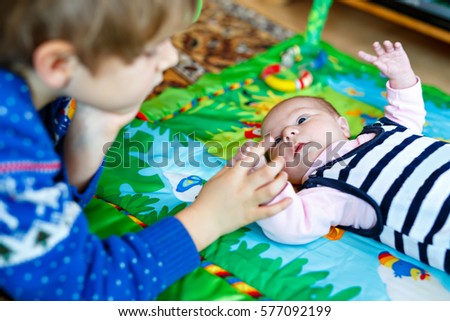 Happy little kid boy with newborn baby girl, cute sister. Siblings. Brother and baby playing with colorful toys and rattles together. Kids bonding. Family of two bonding, love.