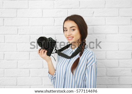 Beautiful young photographer near light brick wall