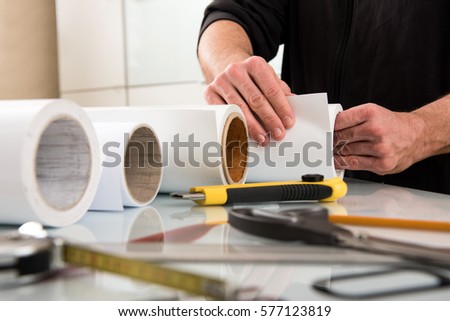 Work of designer in printing house, incognito male hands choosing paper roll for wide format printer, with tools on table in foreground Royalty-Free Stock Photo #577123819