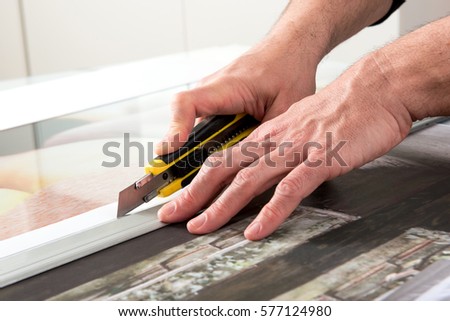 Close-up hands of male professional cutting wide format prints using utility knife cutter Royalty-Free Stock Photo #577124980