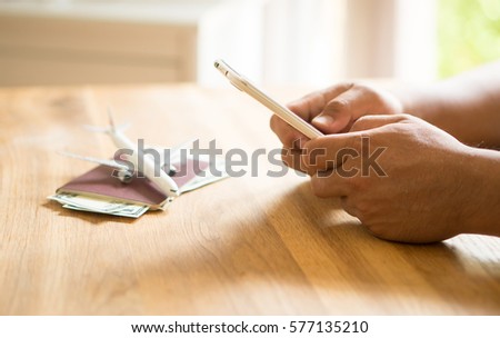 hand holding smart phone with airplane model passport on wooden desk table, Airline Ticket Booking, Travel holiday Concept.