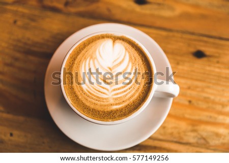 A carefully prepared cappuccino in a simple white cup and plate, sitting on wooden table.