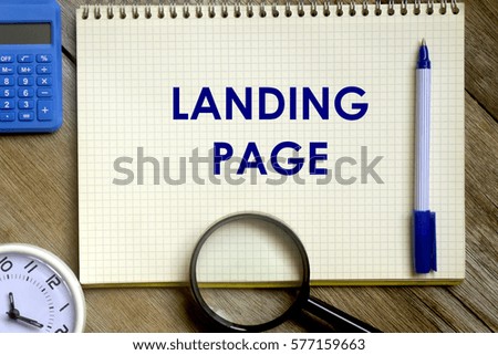 Business concept. Top view of calculator, magnifier, pen, table clock and notebook written LANDING PAGE on wooden background.