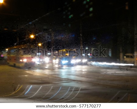 Abstract blurred winter city. Raindrops on a window. Silhouettes urban traffic.