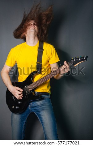 Man with long hair in yellow t-shirt, playing on electric guitar rock. Fashion studio portrait on a gray background. 
Dynamics in the photos, shaking hair.