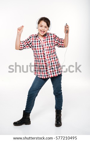 Vertical image of Happy Girl in shirt listening music and dancing. Full length. Isolated gray background
