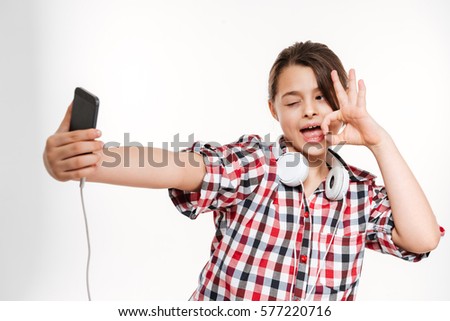 Funny girl in shirt and with headphone making selfie on her phone and showing peace sign