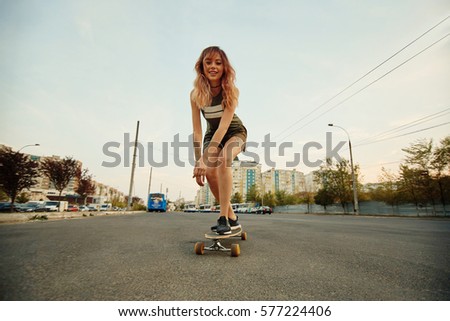 Beautiful young girl with tattoos riding on his longboard on the road in the city in sunny weather. Extreme sports. Rear view of motion