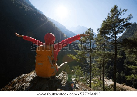 Cheering young woman hiker open arms to sunrise on himalaya mountains