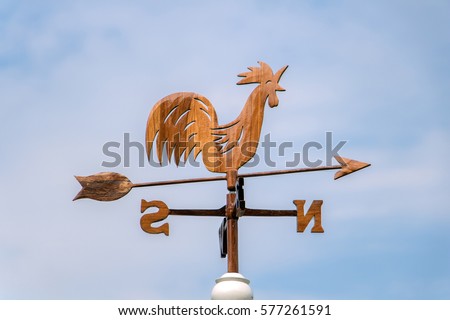 Wooden rooster weather-vane showing a wind direction. Traditional weathercock on heaven background. Decorative cock weathervane close up. Royalty-Free Stock Photo #577261591