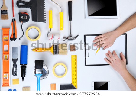 Decorator's hands with pencil and clipboard. Color swatches and tools on work table