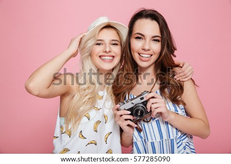 Two smiling pretty young women with old vintage photo camera over pink background