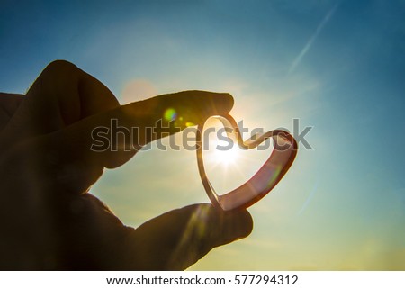 silhouette of Heart Shape in the Hand on the Sky Background. sun rays. Sunset or sunrise. yellow and blue sky. empty copy space for inscription. happy new Valentine's day idea, sign, symbol, concept.