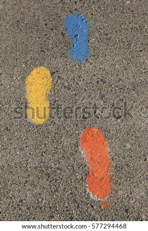 Vertical image of gray cement with painted footprints in blue,yellow and orange.