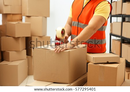 Closeup of man packing parcels with sticky tape at warehouse Royalty-Free Stock Photo #577295401