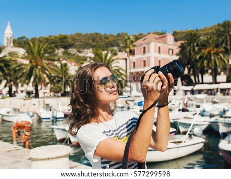 young beautiful woman traveling in Mediterranean, taking pictures on digital photo camera, summer vacation, resort style, sunglasses, sunny, tropical, sightseeing in port