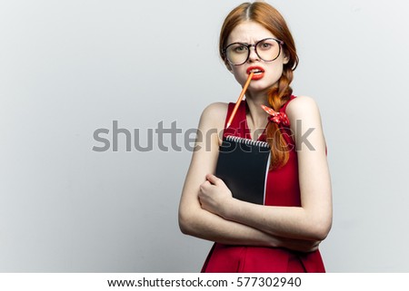 Thoughtful young girl in glasses with a notebook looking at the camera, light background