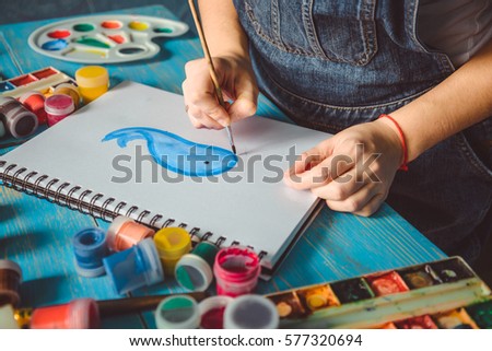 Pretty smiling young woman drawing a picture with whale