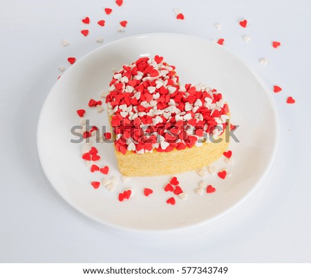 Pile of pancakes in the shape of a heart on white plate with little white and red sugar hearts