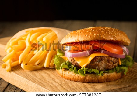 Home made hamburger with beef, onion, tomato, lettuce and cheese. Fresh burger closeup on wooden rustic table with potato fries, beer and chips. Cheeseburger.