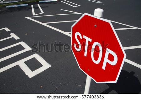 Red and White Stop Sign and Indication Painted on Black Pavement in Parking Lot with Angled Spaces in Background, Angle Facing Left, Bright Sunny Day in February