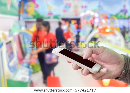 Man use mobile phone, blur image of children play the game in the mall as background.