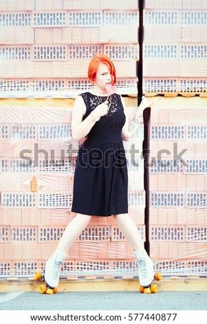 red-haired girl in a black dress in roller skates with candy near the bricks