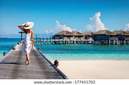 Woman in white walking over a wooden jetty in the Maldives Royalty-Free Stock Photo #577455703