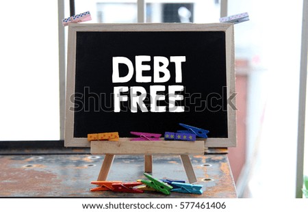 A Concept Image of a blackboard with a word DEBT FREE and a small colorful clothespin on a rusty table surface over a blur bright background