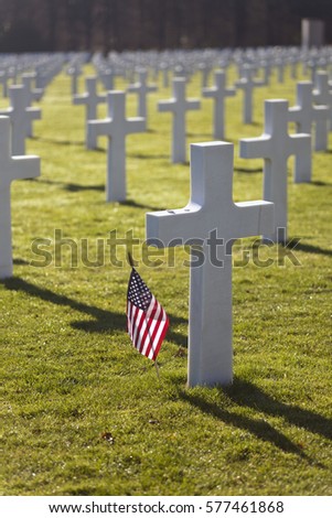 American flag waving next to a cross at the American Cemetery and Memorial near Luxembourg in Europe