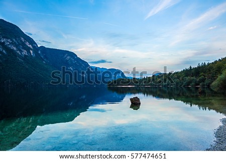 Sunset over lake Bohinj in Triglav National Park, Slovenia. Lake is surrounded by Julian Alps. Beautiful reflections of mountains and trees on smooth surface of water. Quiet natural evening background