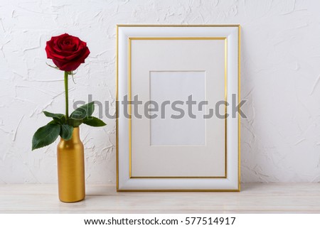 Frame mockup with burgundy red rose in golden  vase.  Empty gold decorated frame mock up for presentation artwork.