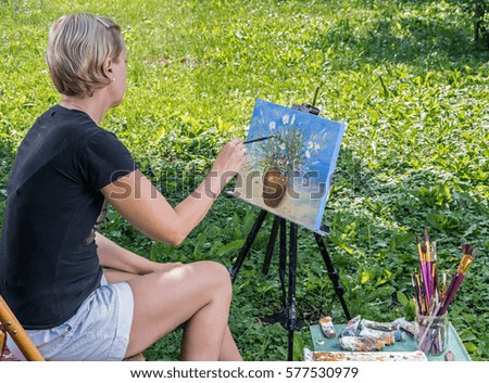 Female artist paints in oil on the open air in a sunny summer day.
