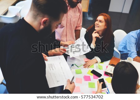 Group of colleagues going over paperwork together in a modern office. Positive way of discussing important questions. Team-workers analyzing together graphs and charts on printed statistic documents
