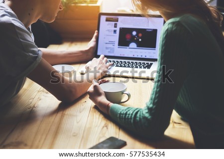 Cropped image of group of young students are watching movie on laptop computer, while are sitting at wooden table in loft. Group of friends using net-book during meet in modern coffee shop interior Royalty-Free Stock Photo #577535434