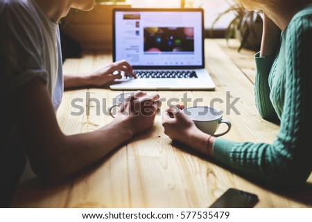 Close up view of hipster friends watching video in social network via portable net-book, while sitting at wooden table in coffee shop. Group of people are reading news information on laptop computer Royalty-Free Stock Photo #577535479