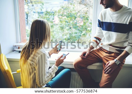 Male and female young bloggers trying to make photo and video posts on social networks sharing information with followers via modern smartphones connected to fast internet in coworking wifi zone area