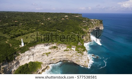 Aerial drone photo of the beautiful seashore where rock meet with powerful ocean waves. View from altitude of Balinese coastline with lighthouse on the edge of a cliff. Amazing nature landscape