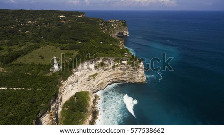 View from the bird's eye view of the beautiful coast of the ocean where rock meet  with powerful waves. Aerial drone photo of beautiful seashore with Balinese coast lighthouse on the edge of a cliff