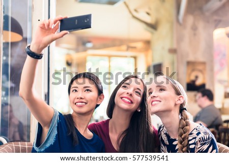 Three beautiful young women smiling while making selfie photos in a restaurant