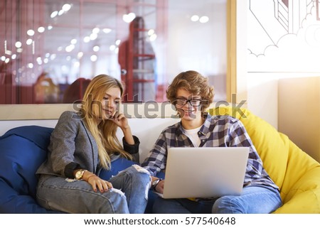 Two young male and female student bloggers waiting for feedback from followers in social network spending free time in coworking space using laptop computer and wireless connection to 4G interne