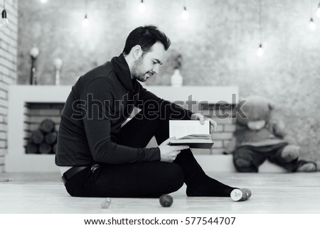 Young man reading a book seated on the floor at home. black and white photo